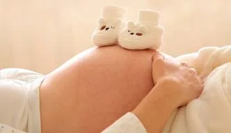 Schwangere Frau mit den Baby-Schuhen auf dem Bauch.