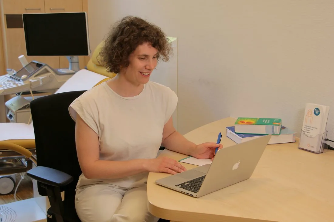 Dr. Anne Bode in einer Onlinesprechstunde sitzend vor einem Laptop in der Fera Praxis.